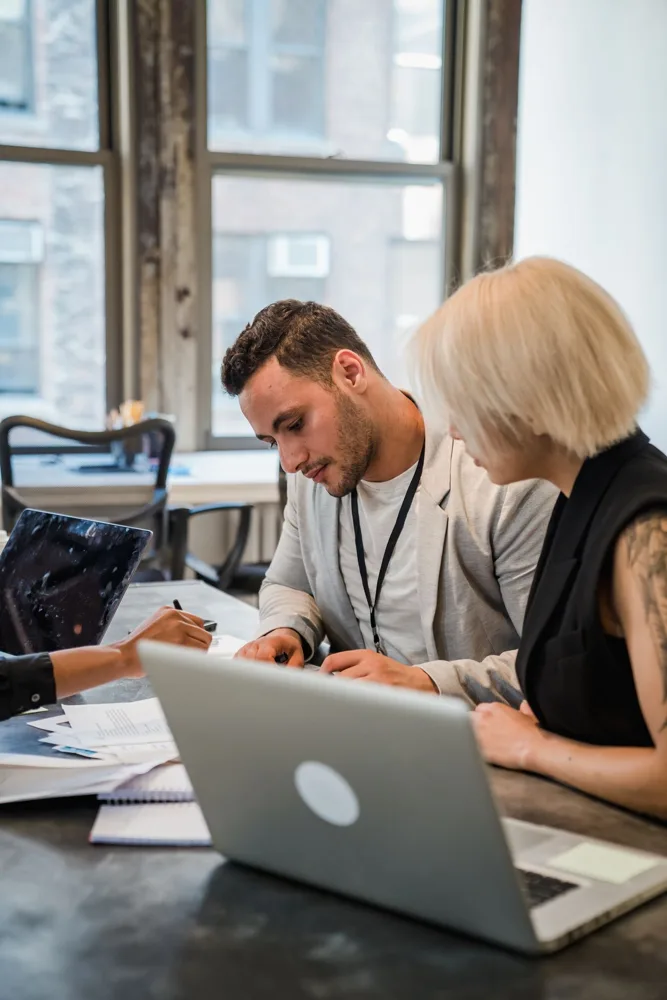 Two coworkers carefully reviewing paperwork beside a laptop