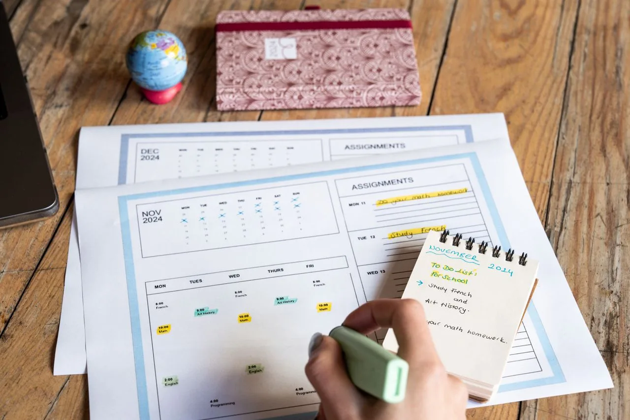 A hand marking tasks on a paper planner and calendar