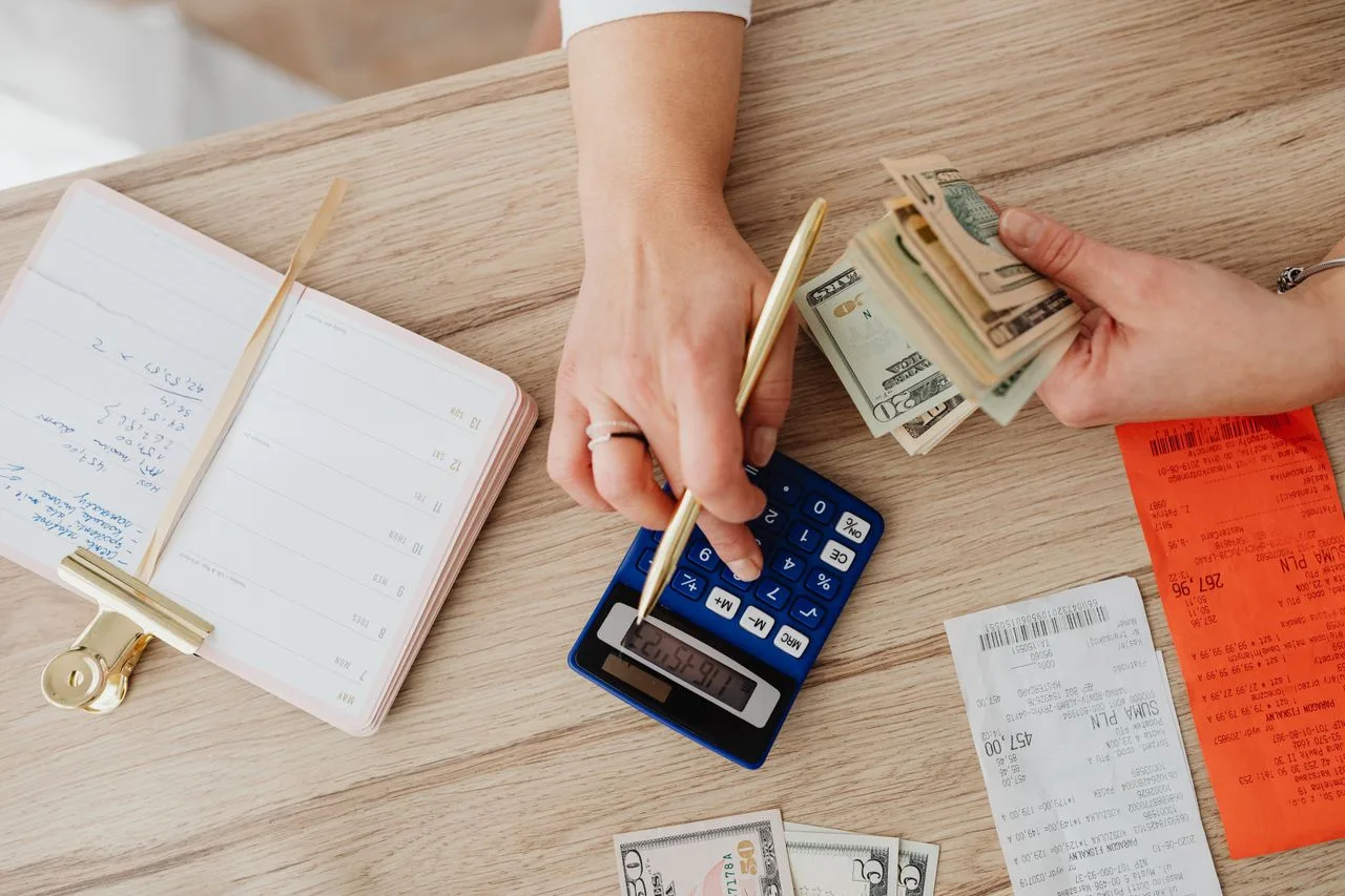 Hands using a calculator beside cash and receipts