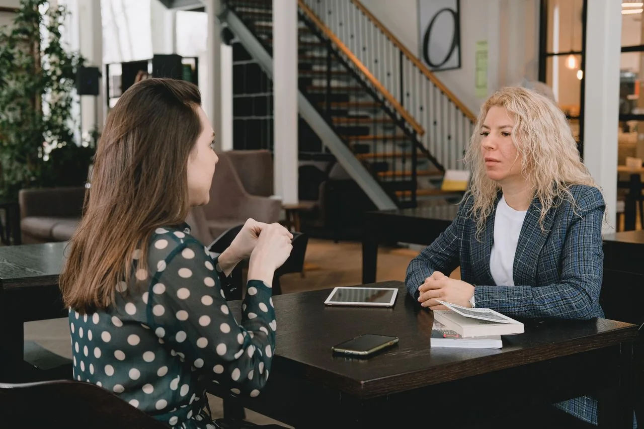Two businesswomen talking across a table with a notebook